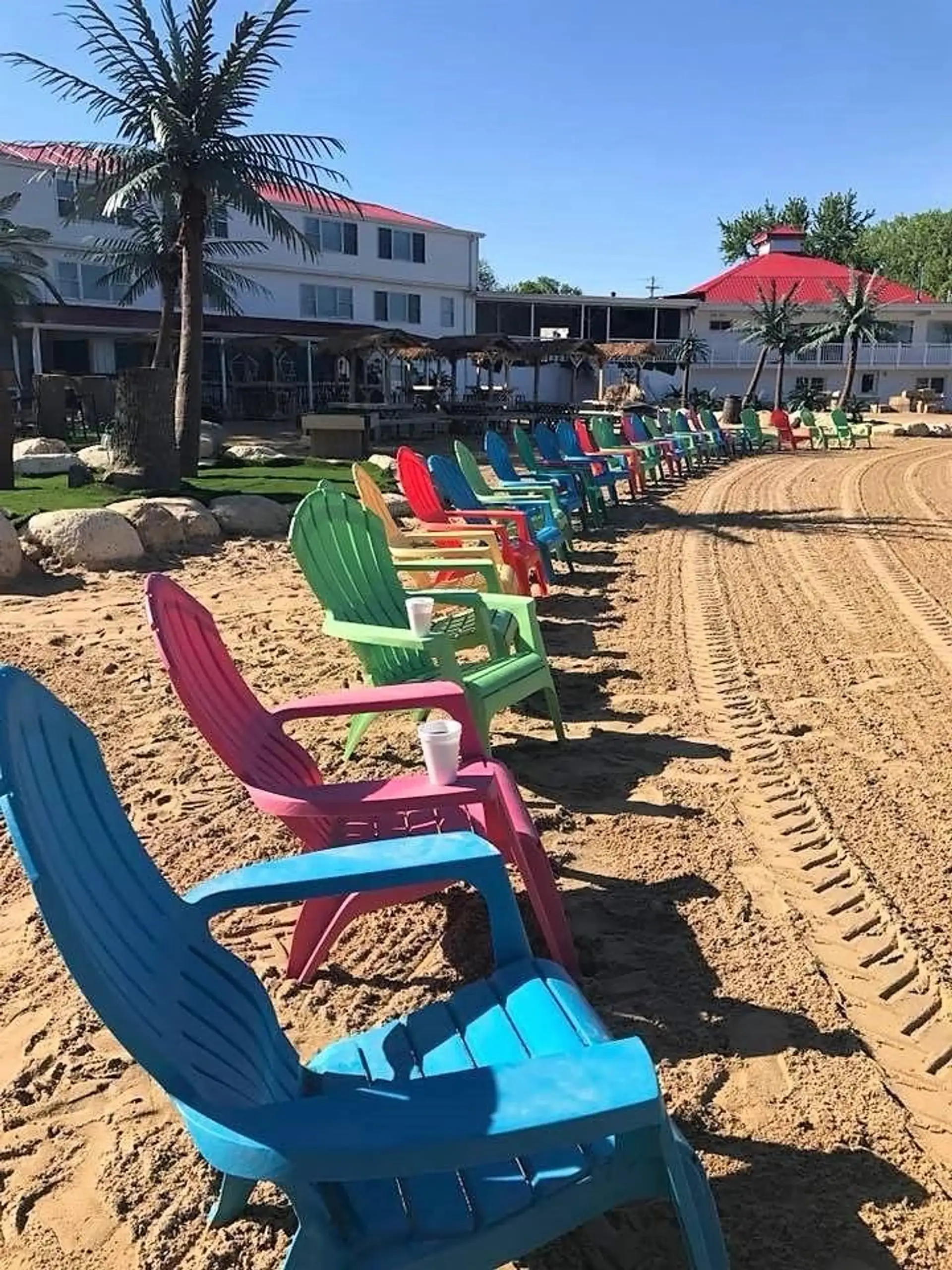 A line of colorful Adirondack chairs down the sand toward the resort