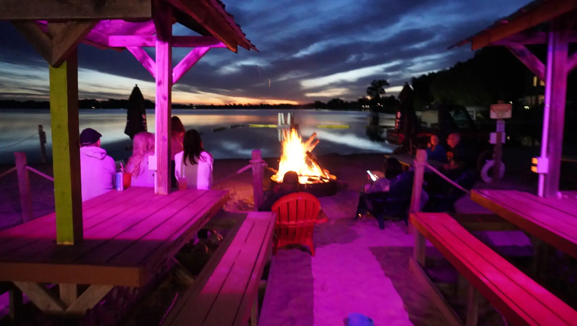 Evening beach bonfire with color-lit tables and guests by the lake